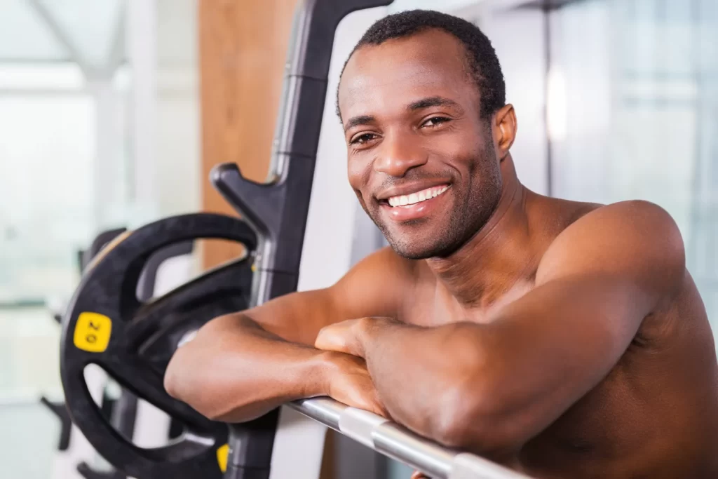 smiling man leaning on barbell rack in gym utc